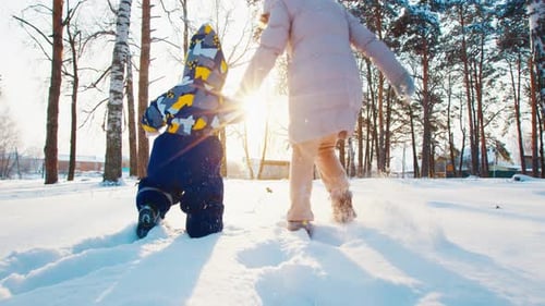 Winter family fun. Young mother runs with her toddler kid in the winter garden