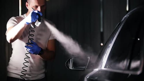 Man sprays cleaning solution onto car side mirror