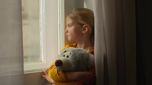 Young Girl Holding Teddy Bear Looking out Window