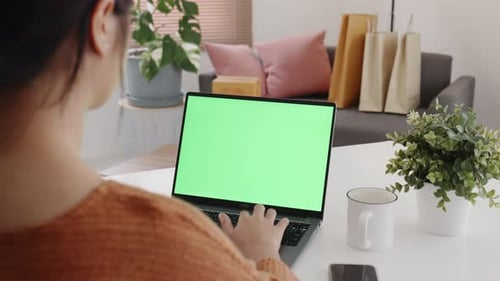 Young Asian woman using laptop computer at home with green blank monitor screen.