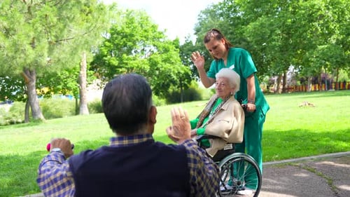 An elderly woman with the nurse on a walk through the garden of a nursing home in a wheelchair and g
