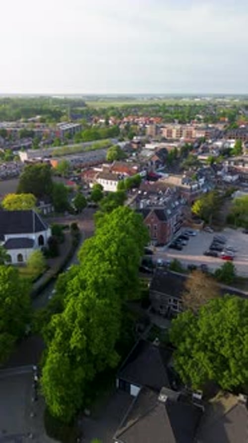 Aerial view of a semi-urban town with dark-roofed buildings, tree-lined streets and open paved areas