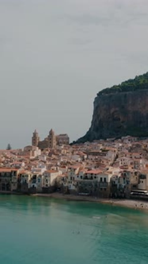 Vertical aerial drone shot of beautiful historic town by the beach. Cefalu sea bay in Sicily. Ancien