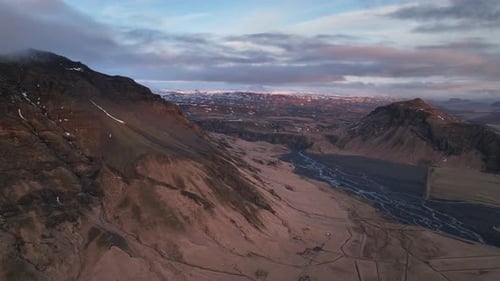Aerial landscape view of a river flowing down from a mountain valley, in Iceland, on a cloudy evenin