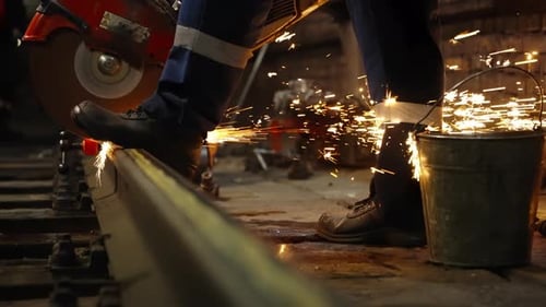 Industrial Railway Maintenance Scene with a Worker Cutting a Steel Rail Using a Powerful Abrasive