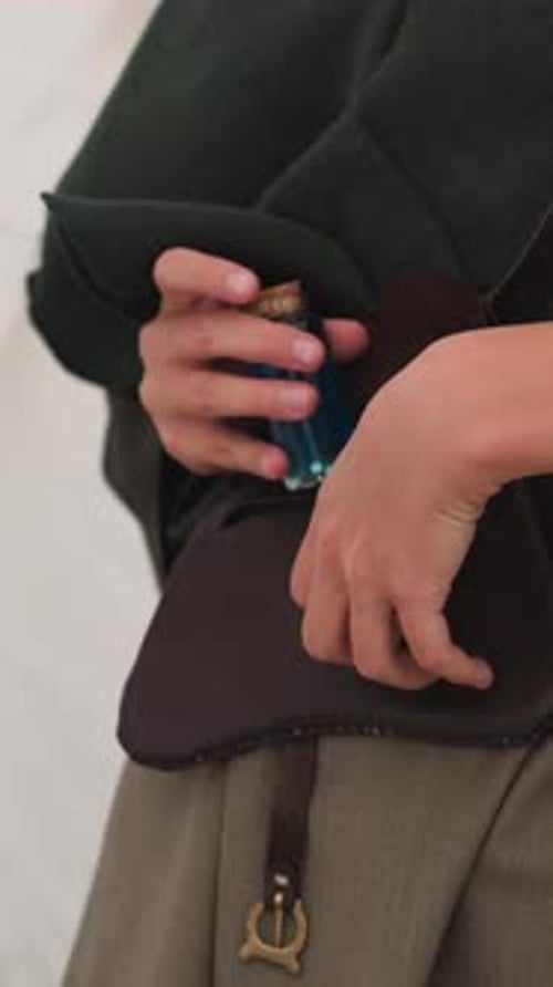 Person Puts Blue Vial in Leather Bag