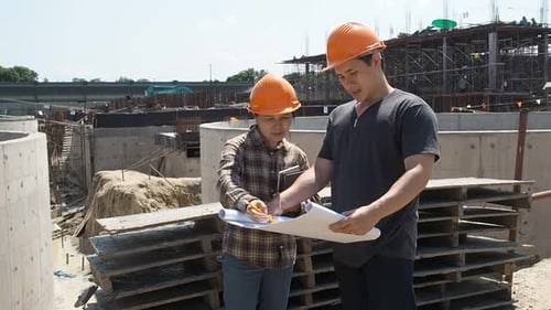 Construction manager and engineer discussing and checking plans on construction site.