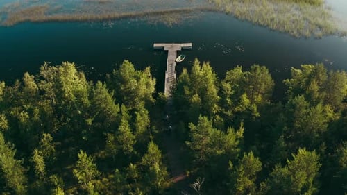 Drone Flies Over a Huge Blue Lake with Long Wooden Pier and Boat Among Forests