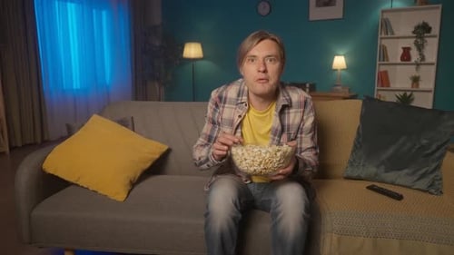 Horror Film Shocked Man Watching a Scary Movie on TV at Home and Eating Popcorn The Man Shudders in