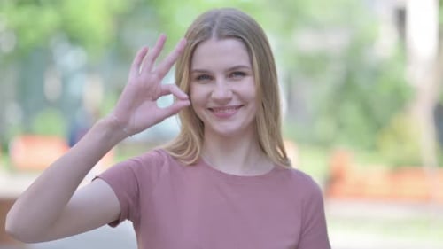 Retrato al aire libre de una mujer joven haciendo el signo Ok