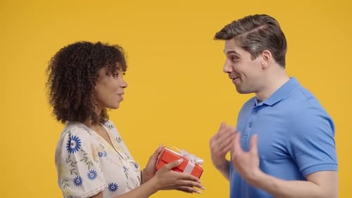 Woman Gives Gift to Smiling Man on Yellow Backdrop