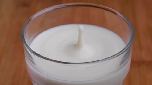 slow motion of a drop of milk splashing into a glass of milk on a table, close up from above, static