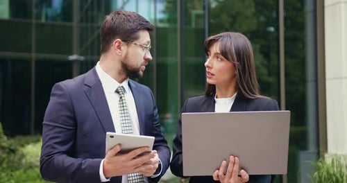 Businessman and Businesswoman having a serious outdoor meeting, discussing important work topics usi
