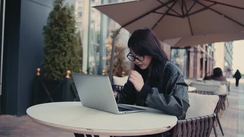 Young Woman Freelancer Working on Laptop at Outdoor Cafe and Feeling Tired