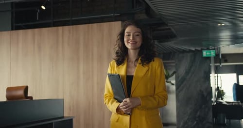 Young and Confident Businesswoman Walking in Office with Notebook