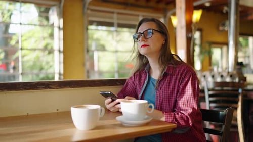 Woman is Using Smartphone and Drinking Coffee in the Cafe