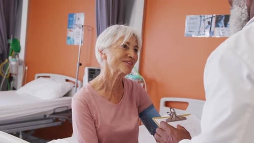 African american male doctor taking blood pressure of senior caucasian female patient at hospital