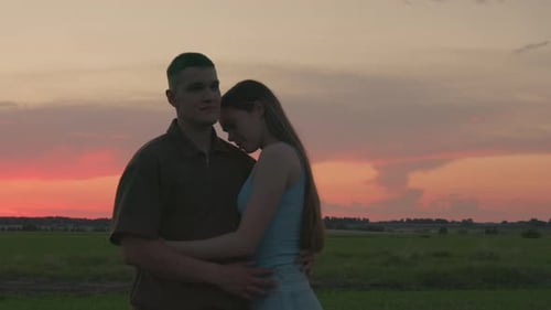 Young Couple Embracing During Peaceful Sunset in Open Field