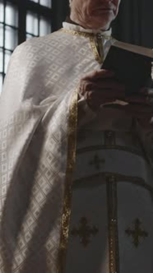 Old Priest in Ornate White Robe Reading Bible aloud in Church