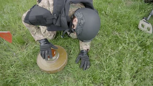 Military sapper demining an anti-tank mine in the field near the forest