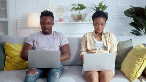 Young couple working on laptops while sitting on couch