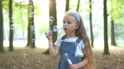 Happy Little Child Girl Blowing Soap Bubbles Outside in Green Park