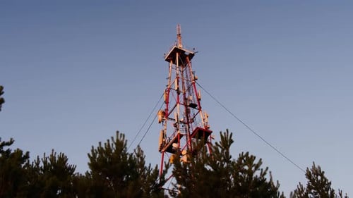 High Red and White Radio Tower in Pine Wood Against Blue Sky