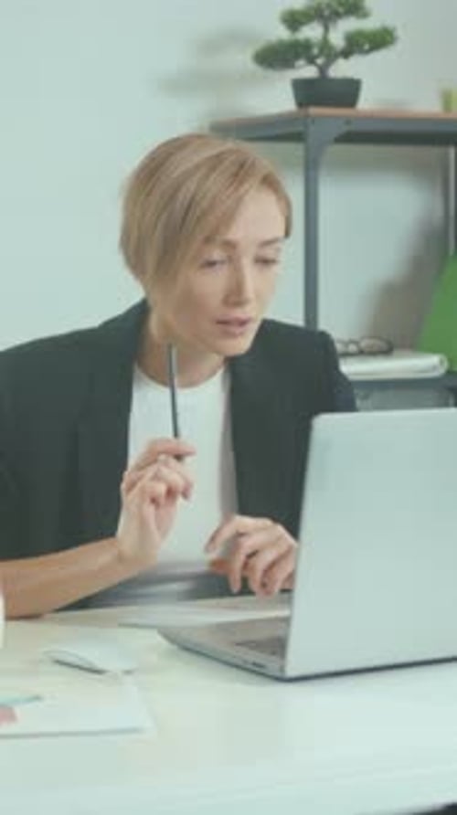 Corporate Consultant Diligently Examining Laptop Content While Taking Notes in Welllit Modern