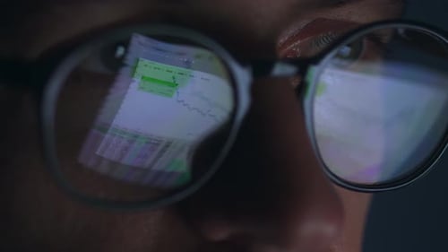 Gros plan de l'œil d'un négociant en bourse de sexe masculin portant des lunettes travaillant à un ordinateur tard dans la nuit