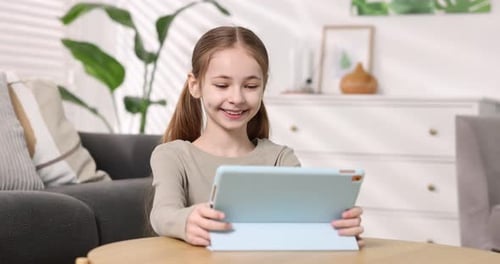 Little girl using tablet at wooden table at home