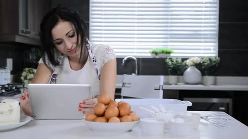Woman Reads Tablet While Baking in Modern Kitchen