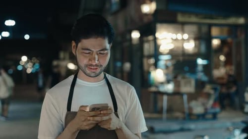 Waiter in Apron Passing By Asian District with Cellphone