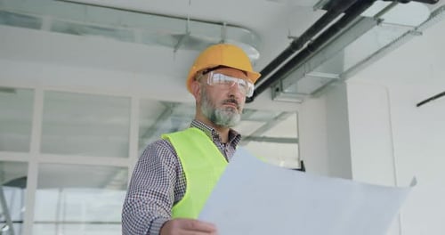 Construction Worker Reviews Blueprint in Workplace