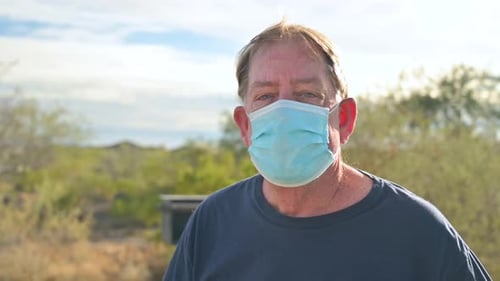 Senior male outdoors in nature, wears face mask during Coronavirus Covid19 pandemic and Delta and Om