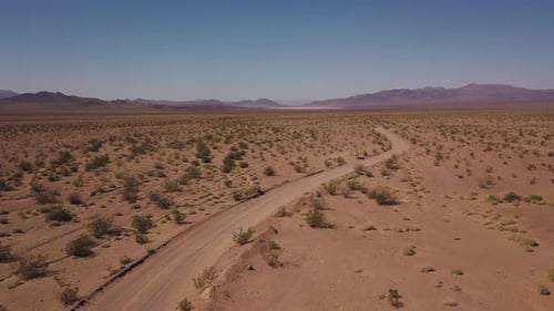Desert dirt road leading to a mountain range in the distance, winding single track - Drone push forw