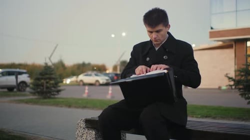 Businessman Going Through Documents Outdoors After Work with City Background