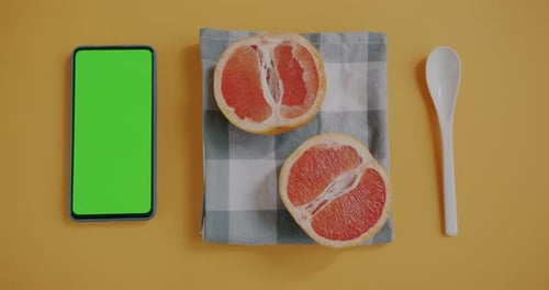 Top View of Grapefruit Half with Spoon and Chroma Key Green Screen Smartphone on Yellow Color