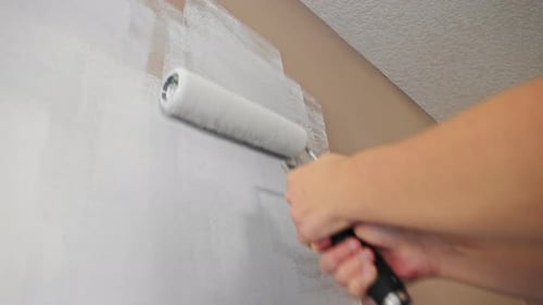 Close up of a caucasian person painting a wall white with a paint roller using both hands.