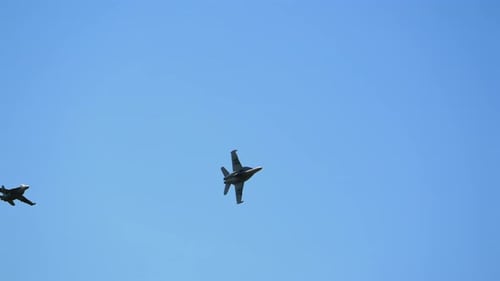 Two fighter jets fly across partly cloudy sky