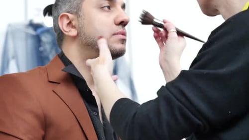 A Male Model Receiving a Professional Makeup Application in a Stylish Studio Setting