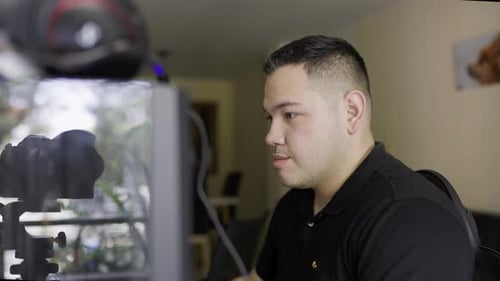 mittelenge Aufnahme eines weißen jungen Latino-Mannes, der an einem Desktop-Computer arbeitet und währenddessen Kaffee trinkt