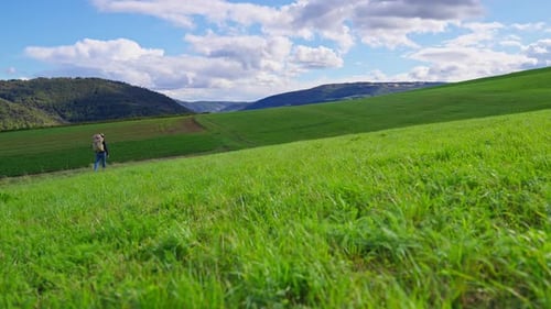 Beautiful green grassy meadow on rolling hills with a hiker walking in the distance on a sunny day