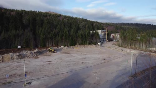 Flying over a prepared ground for a construction site with a bulldozer and forest at the end of the