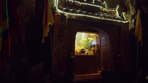 Brightly lit Shrine framed by detailed Stone Arch inside dark Cave with flowers and offerings