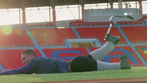 Sport man athlete prosthesis legs lie down on grass field in stadium and exercise to warm up