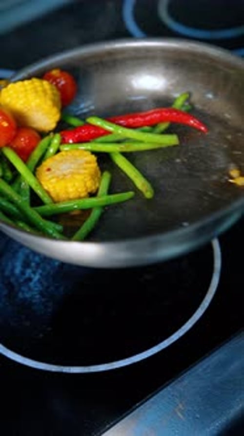 Preparation of vegetables on the frying pan. The pan is moved to mix the veggies. Close up.