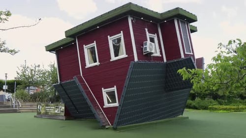 Upside-down red house with white trim and green roof in a park setting