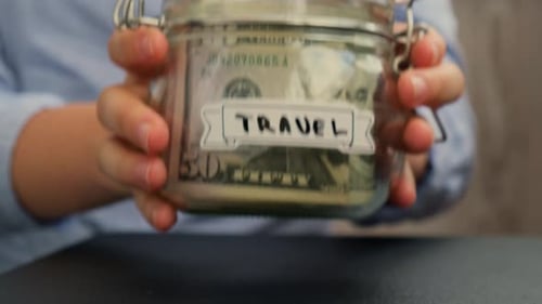 Unrecognizable Woman Put on Table Saving Money In Glass Jar Filled with Dollars Banknotes TRAVEL