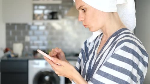 Woman in robe using phone in kitchen