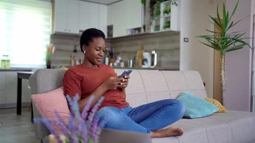 Woman Relaxing on Sofa Using Mobile Phone Indoors